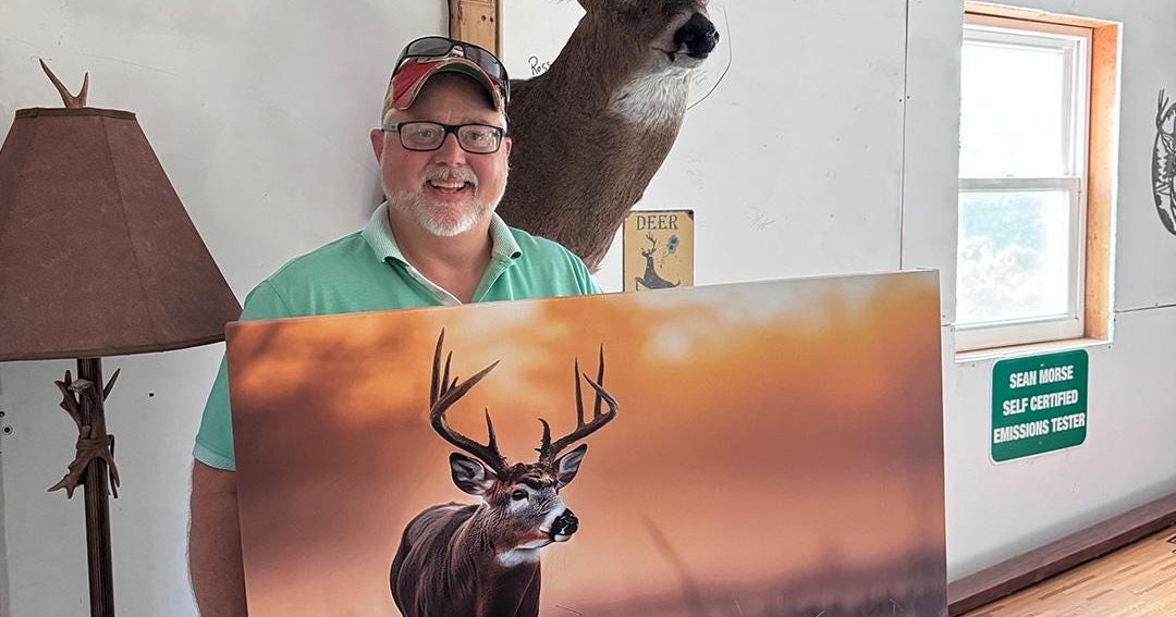 A Hunt Local customer holding his finished virtual taxidermy canvas print of his whitetail buck, next to his real shoulder mount